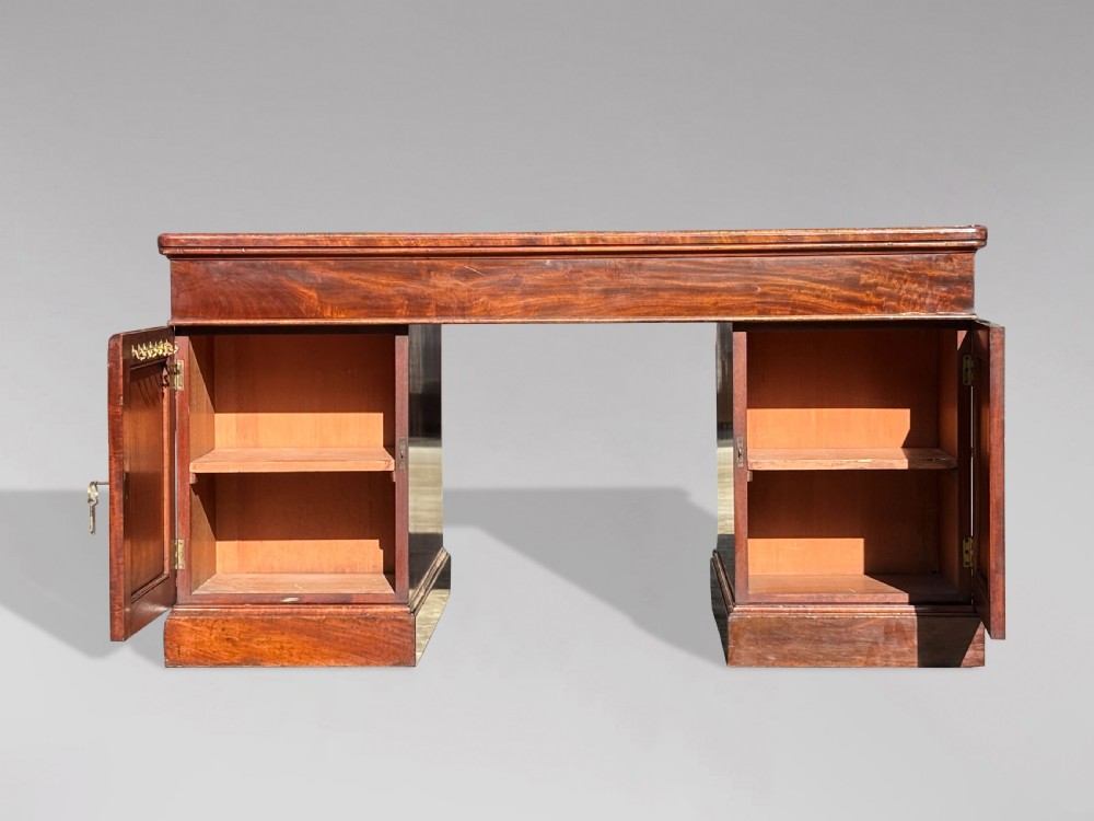 A Victorian flame mahogany partners desk featuring a brown leather inset writing surface, multiple drawers with brass knob handles on twin pedestals, resting on plinth bases. View X