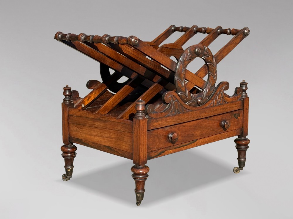 A 19th-century Regency rosewood Canterbury featuring slatted music dividers, carved laurel wreath side handles, a single base drawer, and turned legs with brass castors.