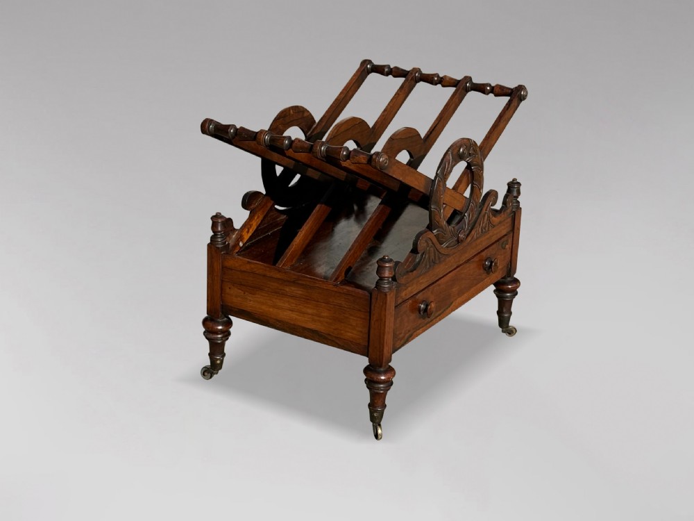 A 19th-century Regency rosewood Canterbury featuring slatted music dividers, carved laurel wreath side handles, a single base drawer, and turned legs with brass castors. View III