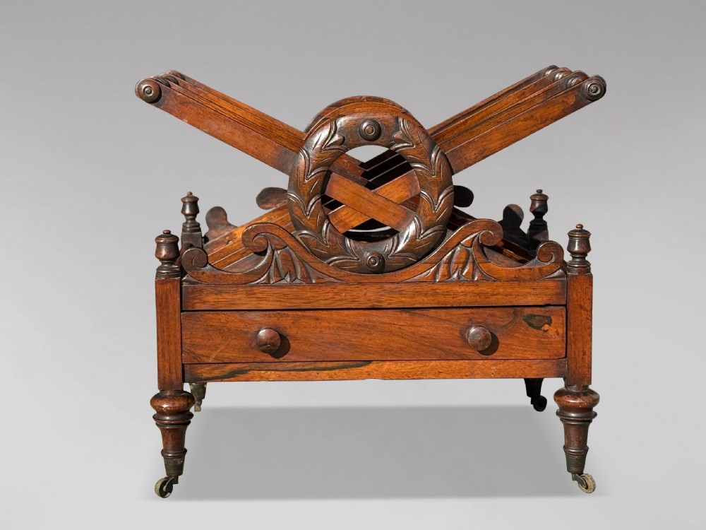 A 19th-century Regency rosewood Canterbury featuring slatted music dividers, carved laurel wreath side handles, a single base drawer, and turned legs with brass castors. View IV