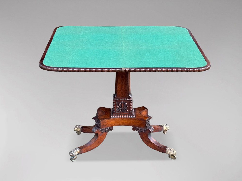 A 19th-century George IV period rosewood fold-over card table featuring a figured veneer top, carved pedestal base, and four splayed legs with brass paw castors. View III
