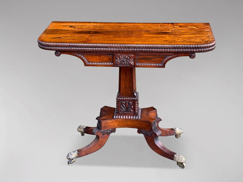 A 19th-century George IV period rosewood fold-over card table featuring a figured veneer top, carved pedestal base, and four splayed legs with brass paw castors. View VIII