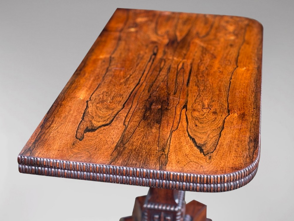 A 19th-century George IV period rosewood fold-over card table featuring a figured veneer top, carved pedestal base, and four splayed legs with brass paw castors. View IX