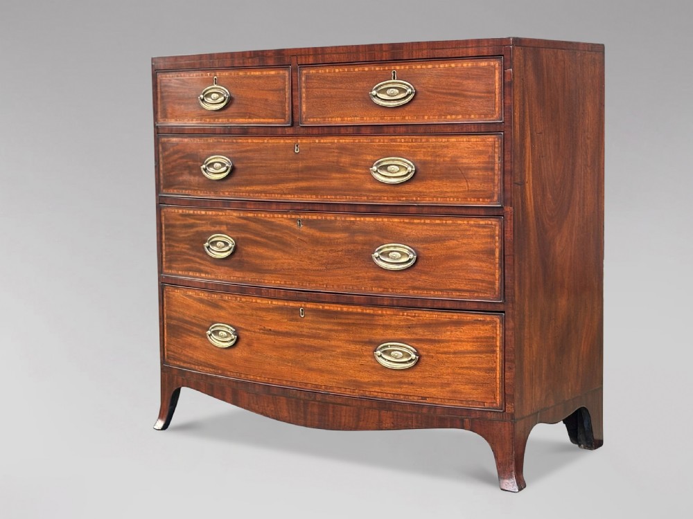 A 19th-century mahogany chest of drawers featuring two short over three long drawers, crossbanded inlay, oval brass handles, and splayed bracket feet.