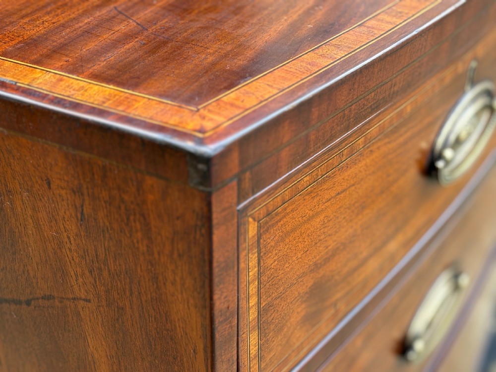 A 19th-century mahogany chest of drawers featuring two short over three long drawers, crossbanded inlay, oval brass handles, and splayed bracket feet. View V