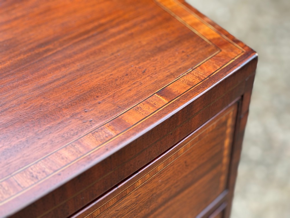 A 19th-century mahogany chest of drawers featuring two short over three long drawers, crossbanded inlay, oval brass handles, and splayed bracket feet. View VI