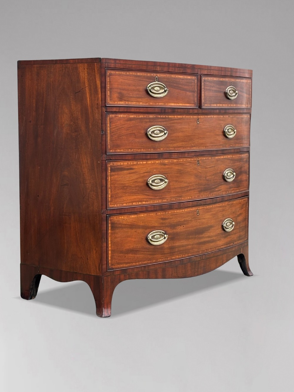 A 19th-century mahogany chest of drawers featuring two short over three long drawers, crossbanded inlay, oval brass handles, and splayed bracket feet. View VIII