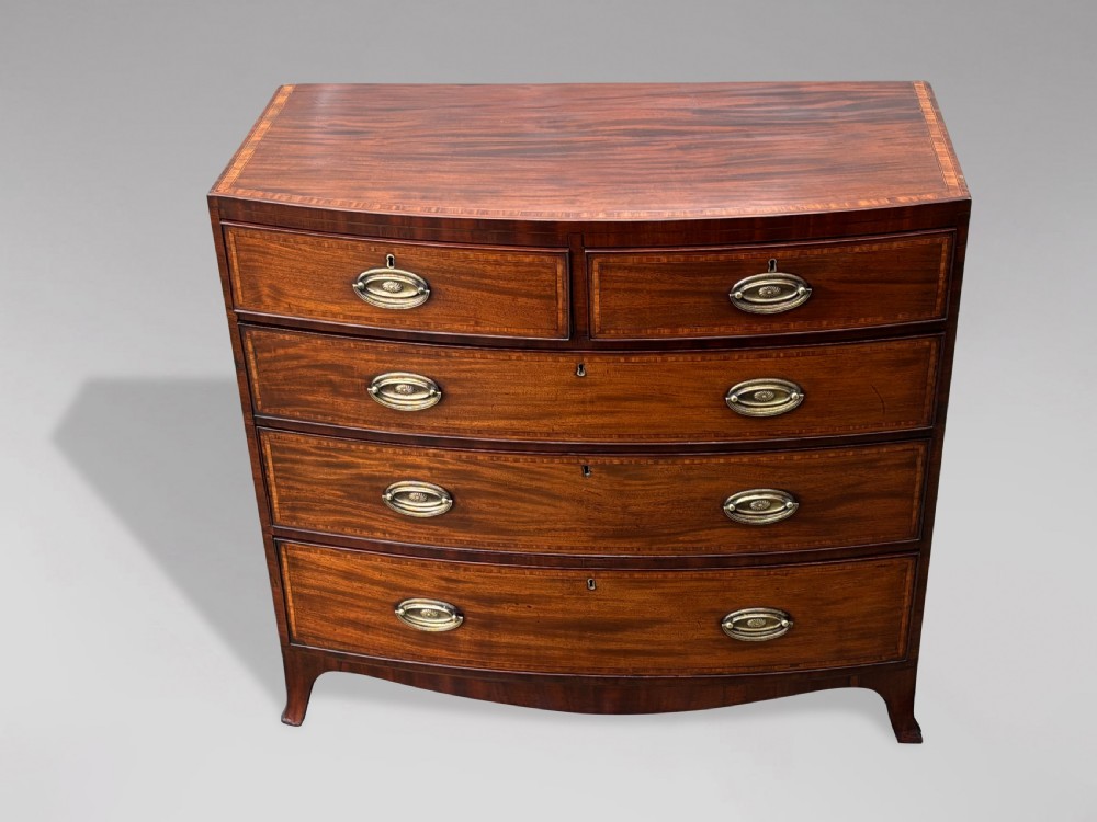 A 19th-century mahogany chest of drawers featuring two short over three long drawers, crossbanded inlay, oval brass handles, and splayed bracket feet. View X