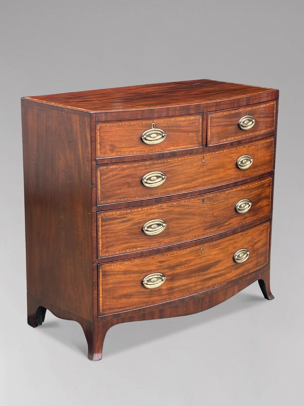 A 19th-century mahogany chest of drawers featuring two short over three long drawers, crossbanded inlay, oval brass handles, and splayed bracket feet. View XI