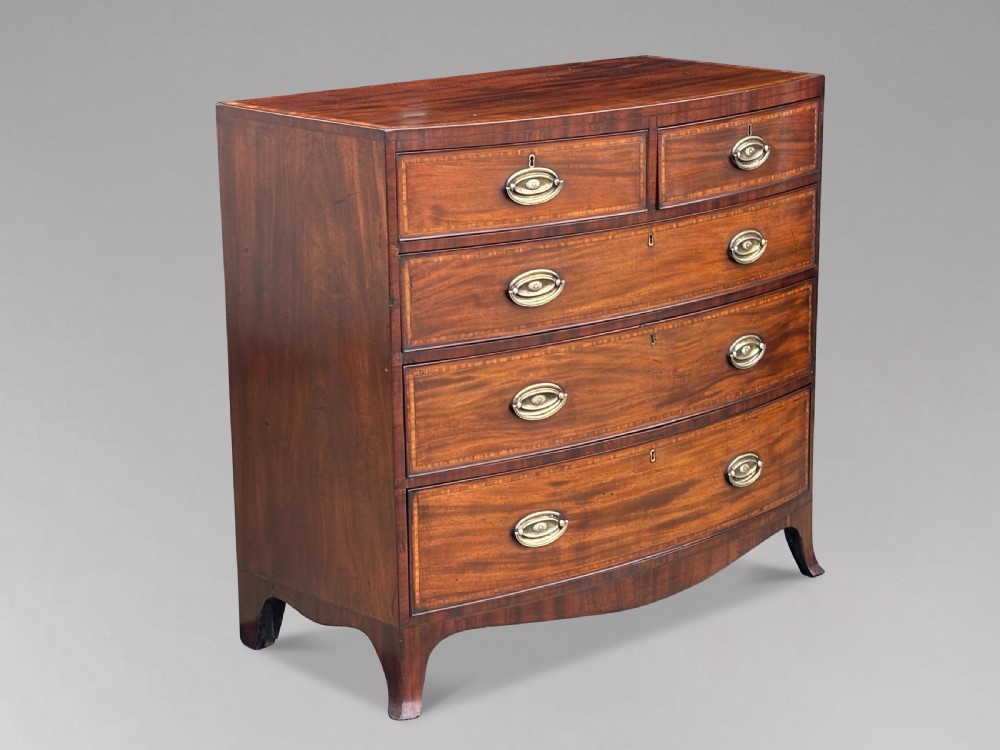 A 19th-century mahogany chest of drawers featuring two short over three long drawers, crossbanded inlay, oval brass handles, and splayed bracket feet. View XII