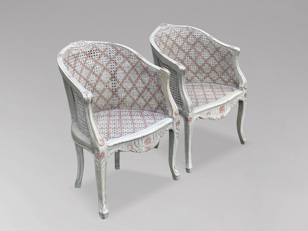 A pair of 20th-century French Louis XV style armchairs with off-white painted frames, pink floral carvings, cabriole legs, and woven cane backs adorned with a painted red diamond pattern. View II