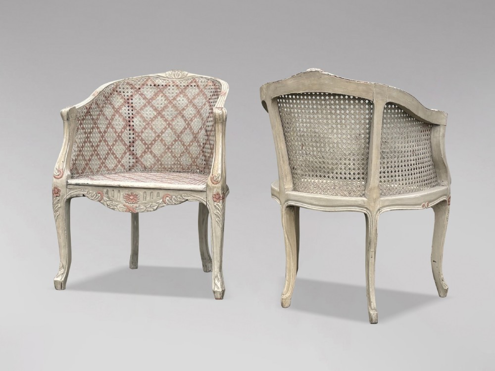 A pair of 20th-century French Louis XV style armchairs with off-white painted frames, pink floral carvings, cabriole legs, and woven cane backs adorned with a painted red diamond pattern. View III