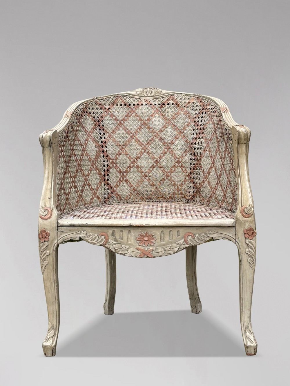 A pair of 20th-century French Louis XV style armchairs with off-white painted frames, pink floral carvings, cabriole legs, and woven cane backs adorned with a painted red diamond pattern. View IV