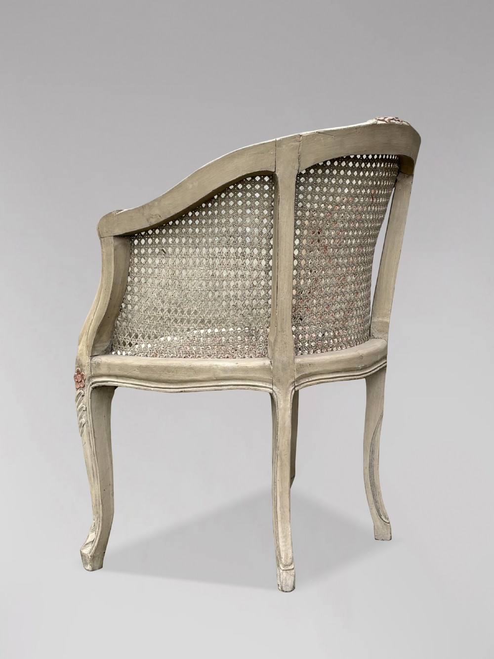 A pair of 20th-century French Louis XV style armchairs with off-white painted frames, pink floral carvings, cabriole legs, and woven cane backs adorned with a painted red diamond pattern. View VI