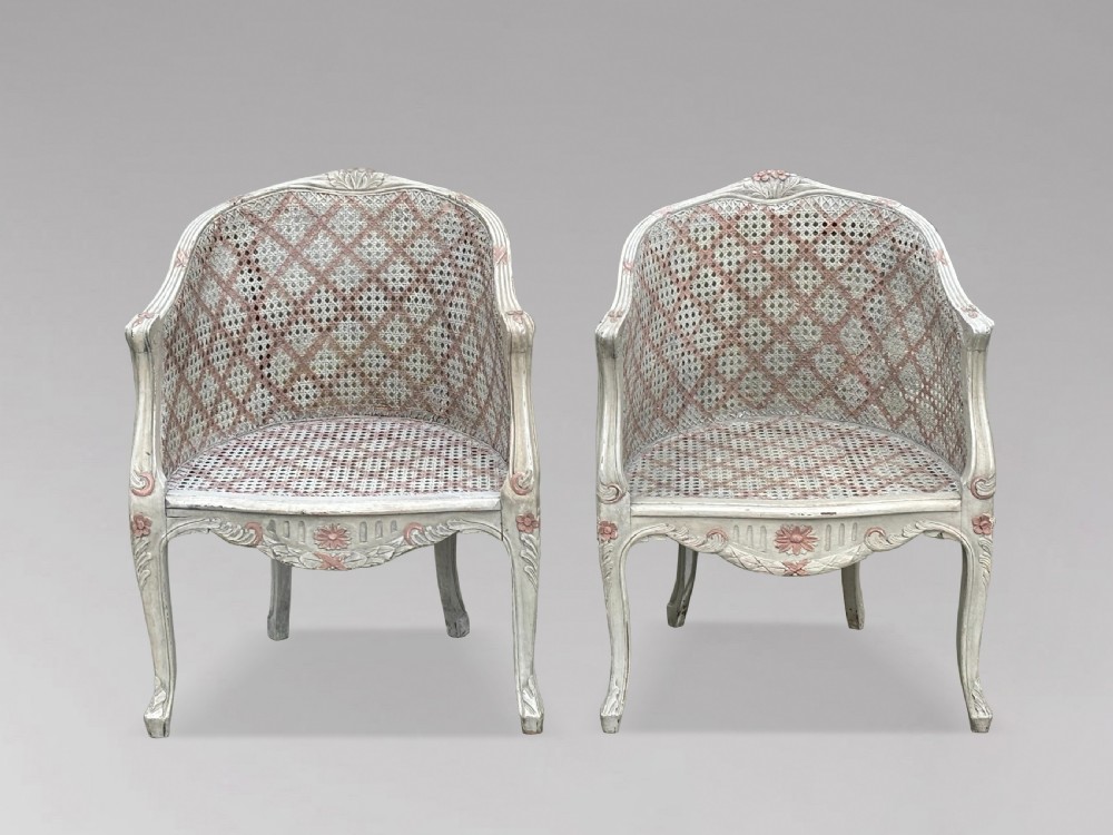 A pair of 20th-century French Louis XV style armchairs with off-white painted frames, pink floral carvings, cabriole legs, and woven cane backs adorned with a painted red diamond pattern. View VII