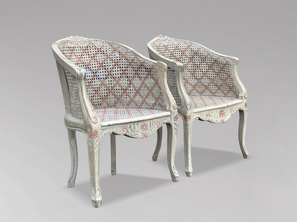 A pair of 20th-century French Louis XV style armchairs with off-white painted frames, pink floral carvings, cabriole legs, and woven cane backs adorned with a painted red diamond pattern. View VIII