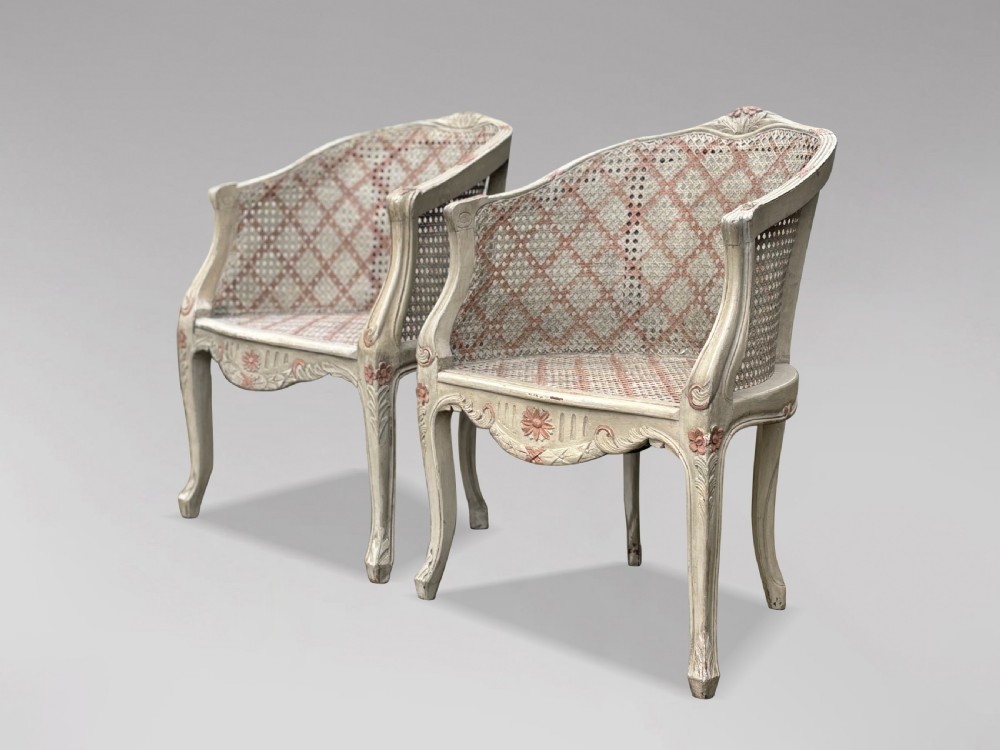 A pair of 20th-century French Louis XV style armchairs with off-white painted frames, pink floral carvings, cabriole legs, and woven cane backs adorned with a painted red diamond pattern. View IX