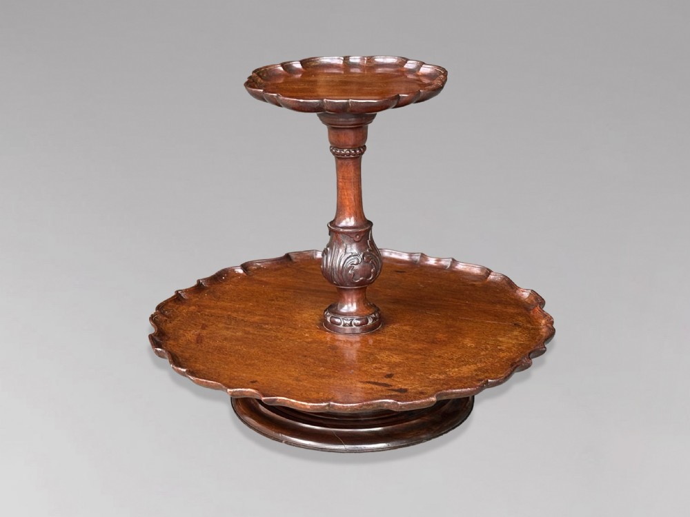 A 19th-century dark brown mahogany two-tier revolving Lazy Susan featuring scalloped piecrust rims and a turned, carved central column.