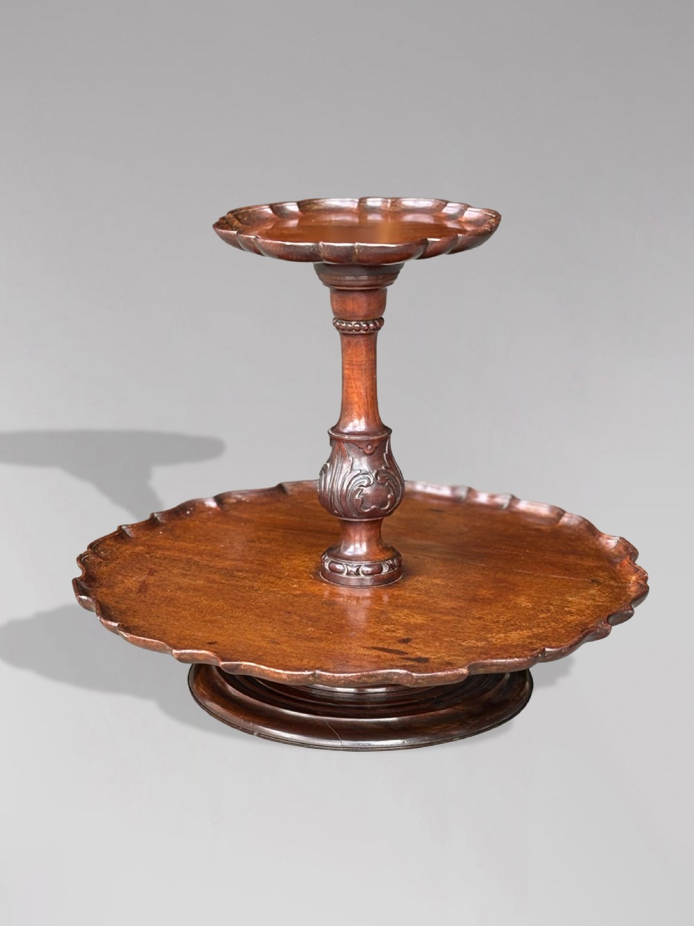 A 19th-century dark brown mahogany two-tier revolving Lazy Susan featuring scalloped piecrust rims and a turned, carved central column. View III