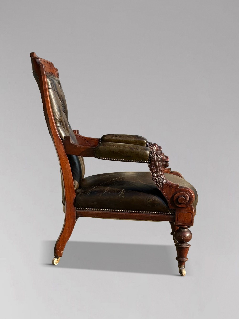 A nineteenth-century carved walnut library armchair with button-tufted dark green leather upholstery, carved lion-head armrests, and turned legs with castors. View II