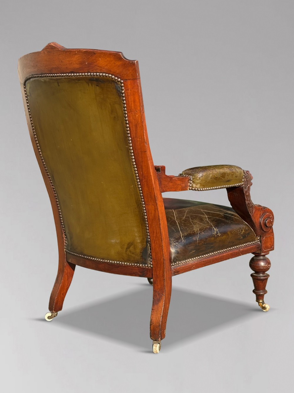 A nineteenth-century carved walnut library armchair with button-tufted dark green leather upholstery, carved lion-head armrests, and turned legs with castors. View III