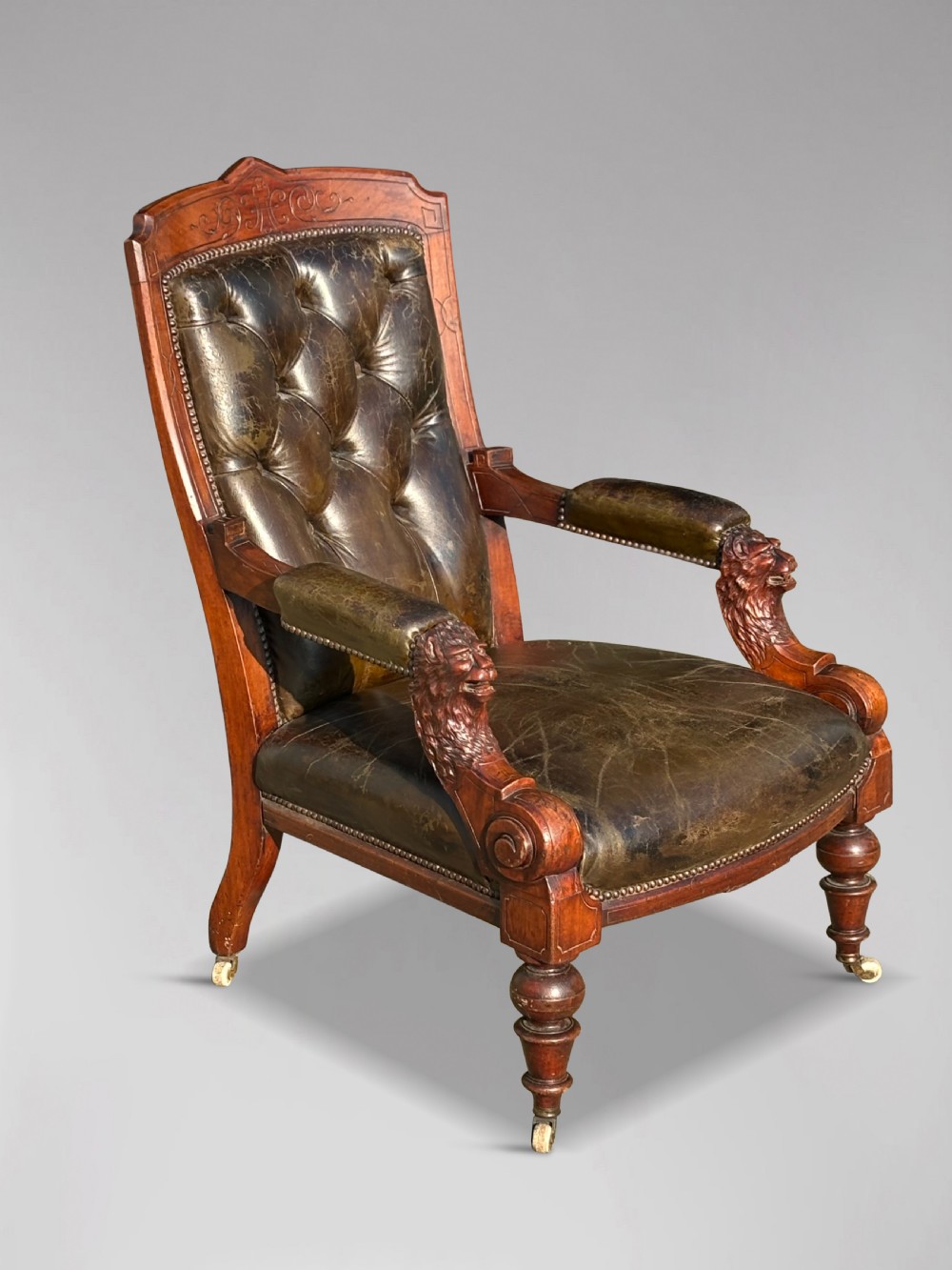 A nineteenth-century carved walnut library armchair with button-tufted dark green leather upholstery, carved lion-head armrests, and turned legs with castors. View IV
