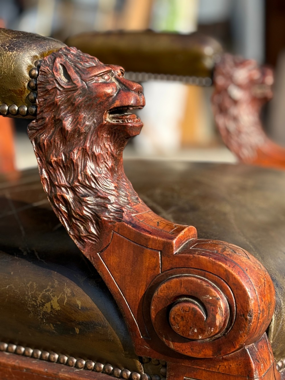 A nineteenth-century carved walnut library armchair with button-tufted dark green leather upholstery, carved lion-head armrests, and turned legs with castors. View V