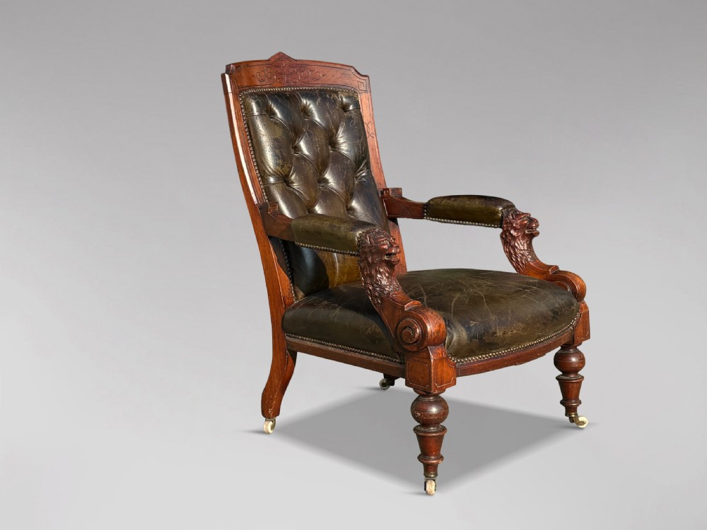 A nineteenth-century carved walnut library armchair with button-tufted dark green leather upholstery, carved lion-head armrests, and turned legs with castors. View X