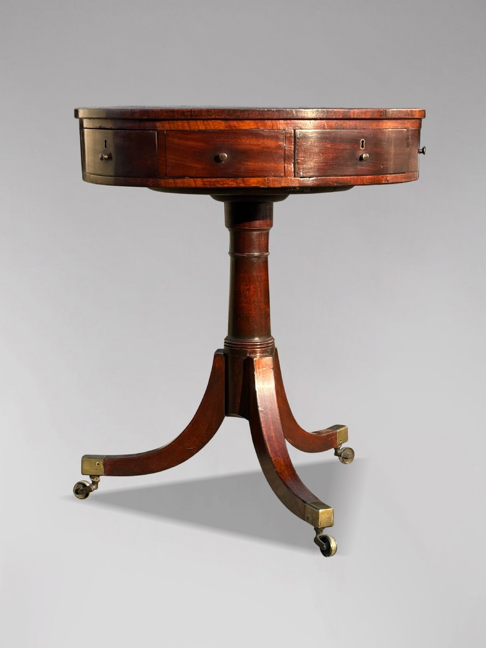 An 18th-century George III mahogany drum table with a circular green leather top, frieze drawers, turned pedestal, and splayed legs with brass castors. View IV