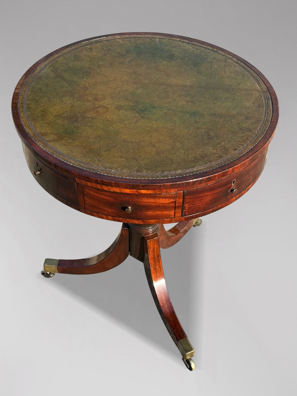 An 18th-century George III mahogany drum table with a circular green leather top, frieze drawers, turned pedestal, and splayed legs with brass castors. View V