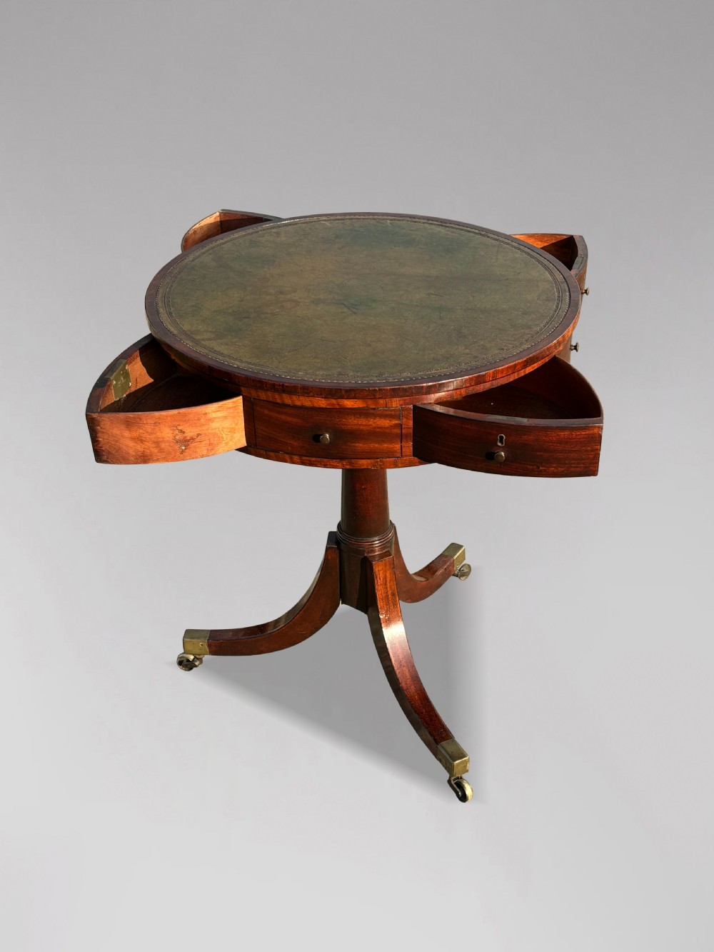 An 18th-century George III mahogany drum table with a circular green leather top, frieze drawers, turned pedestal, and splayed legs with brass castors. View VII