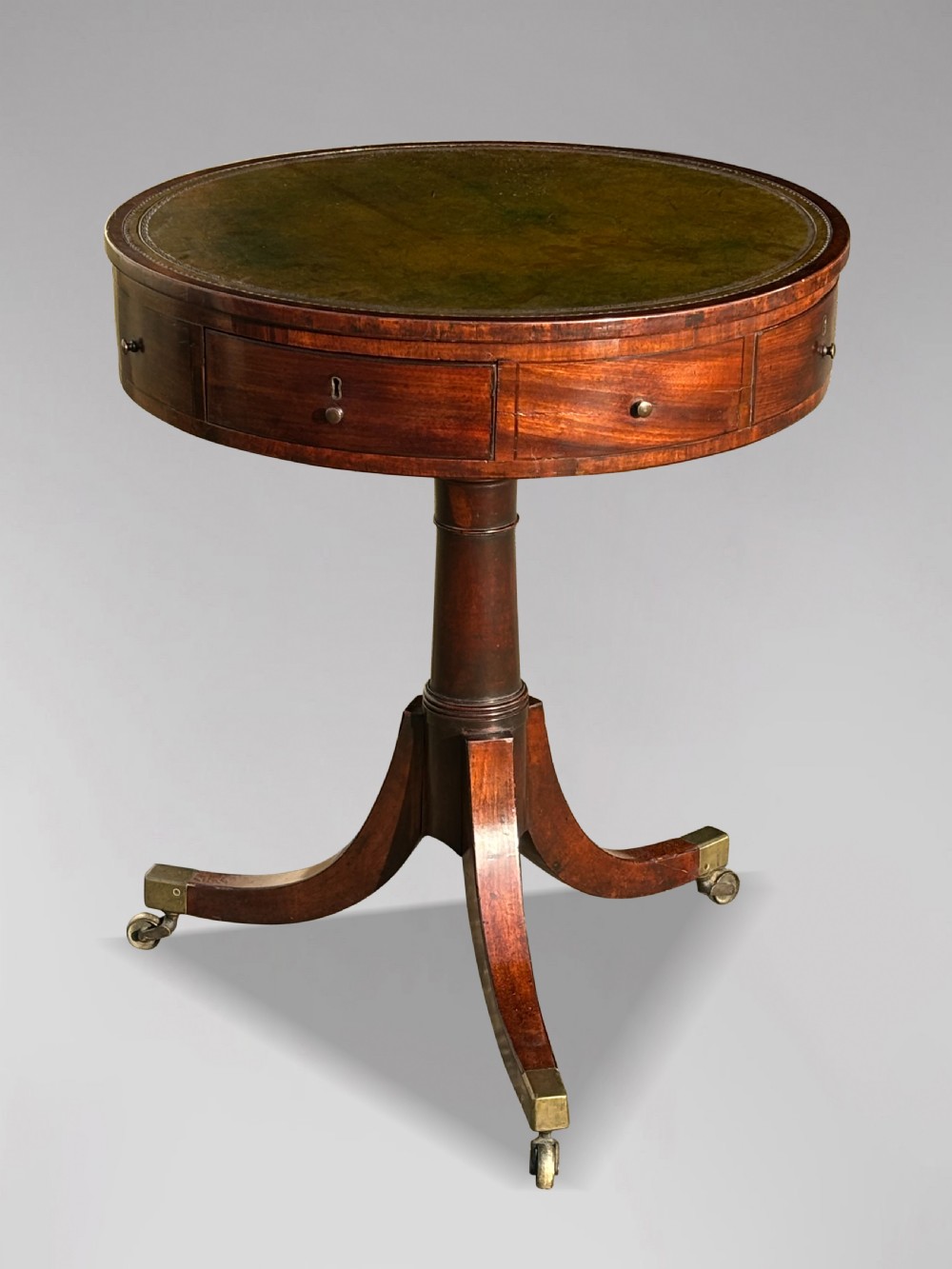 An 18th-century George III mahogany drum table with a circular green leather top, frieze drawers, turned pedestal, and splayed legs with brass castors. View VIII