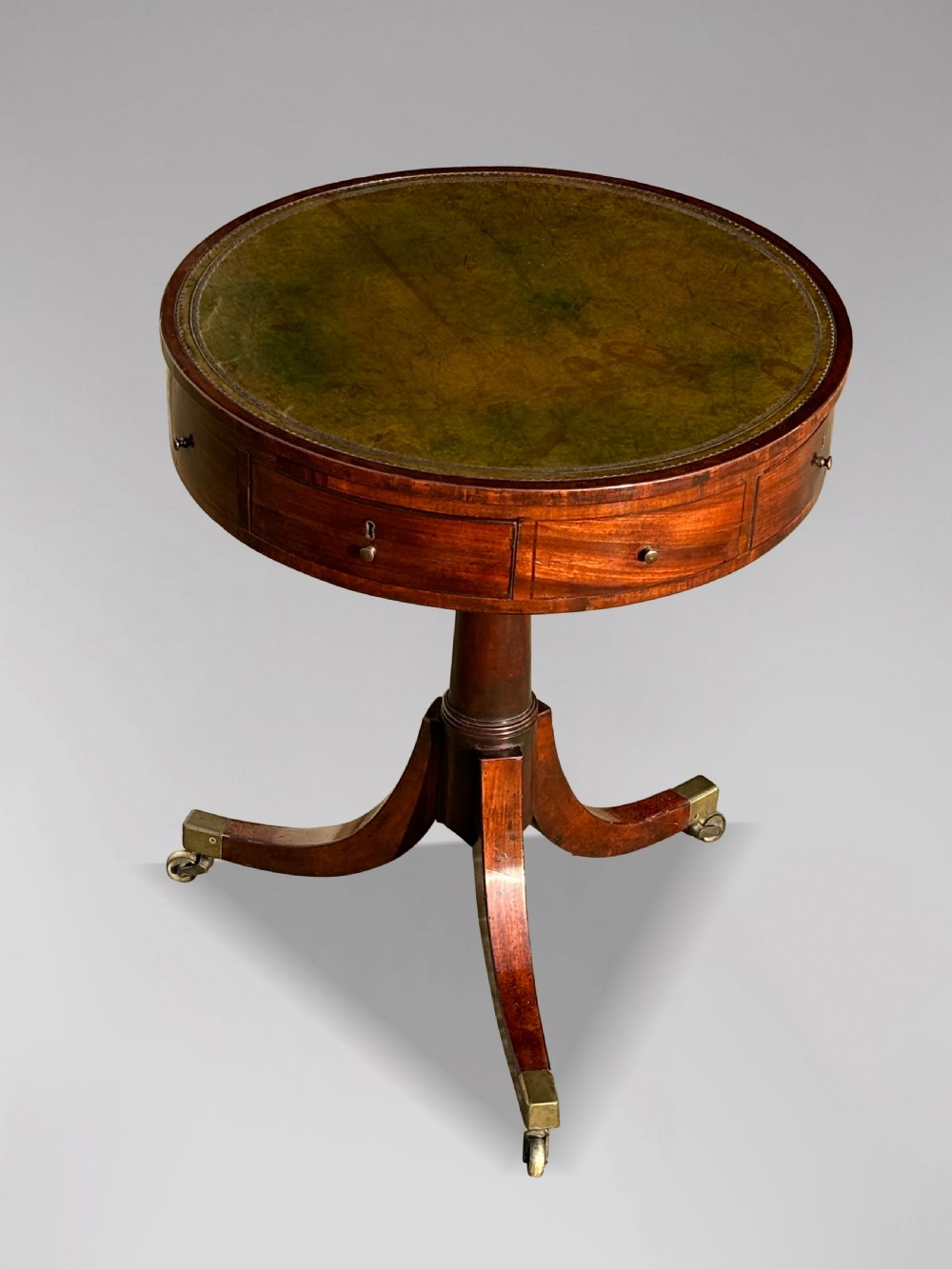 An 18th-century George III mahogany drum table with a circular green leather top, frieze drawers, turned pedestal, and splayed legs with brass castors. View IX