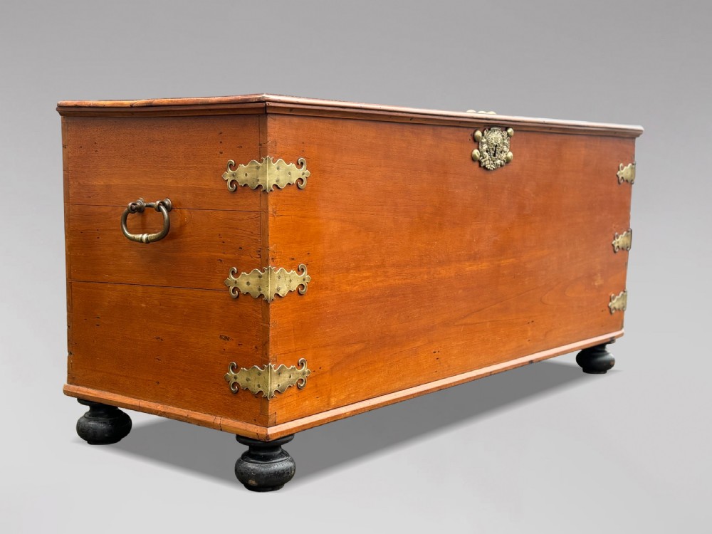 An 18th-century warm brown walnut colonial chest featuring brass corner brackets, a central decorative brass escutcheon, lid studs, and dark turned bun feet. View II