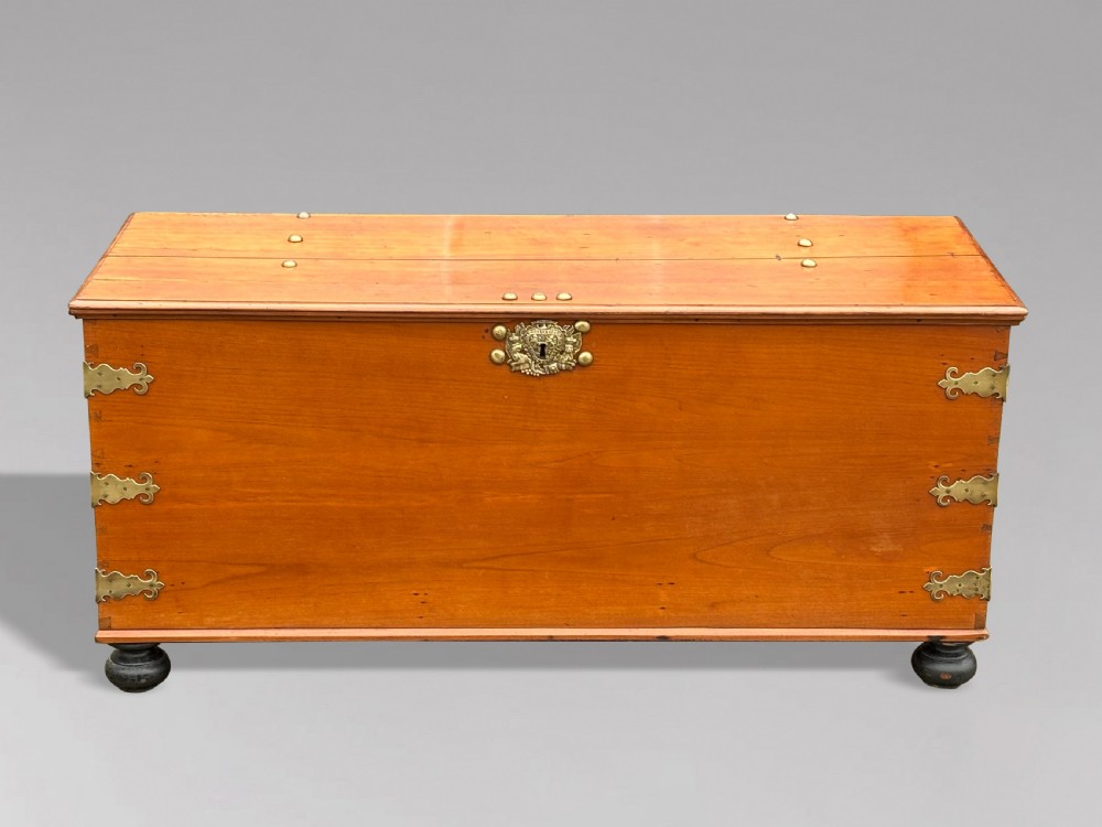 An 18th-century warm brown walnut colonial chest featuring brass corner brackets, a central decorative brass escutcheon, lid studs, and dark turned bun feet. View IV