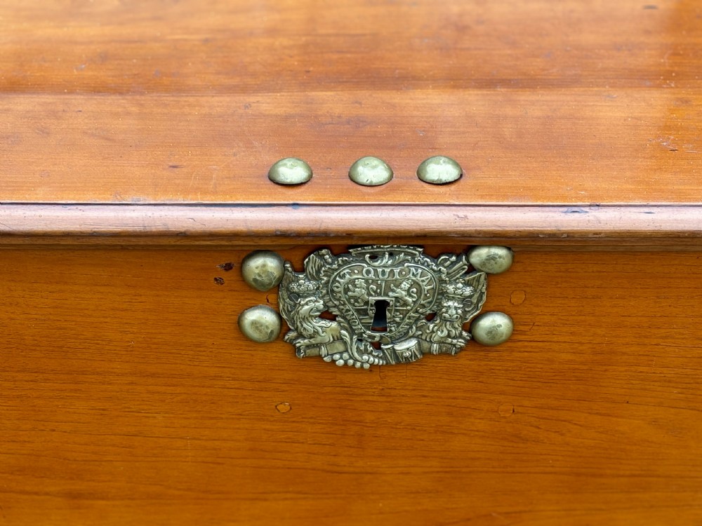 An 18th-century warm brown walnut colonial chest featuring brass corner brackets, a central decorative brass escutcheon, lid studs, and dark turned bun feet. View V