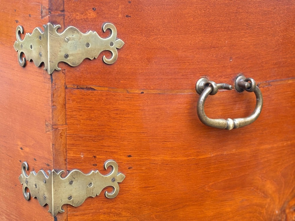 An 18th-century warm brown walnut colonial chest featuring brass corner brackets, a central decorative brass escutcheon, lid studs, and dark turned bun feet. View VII