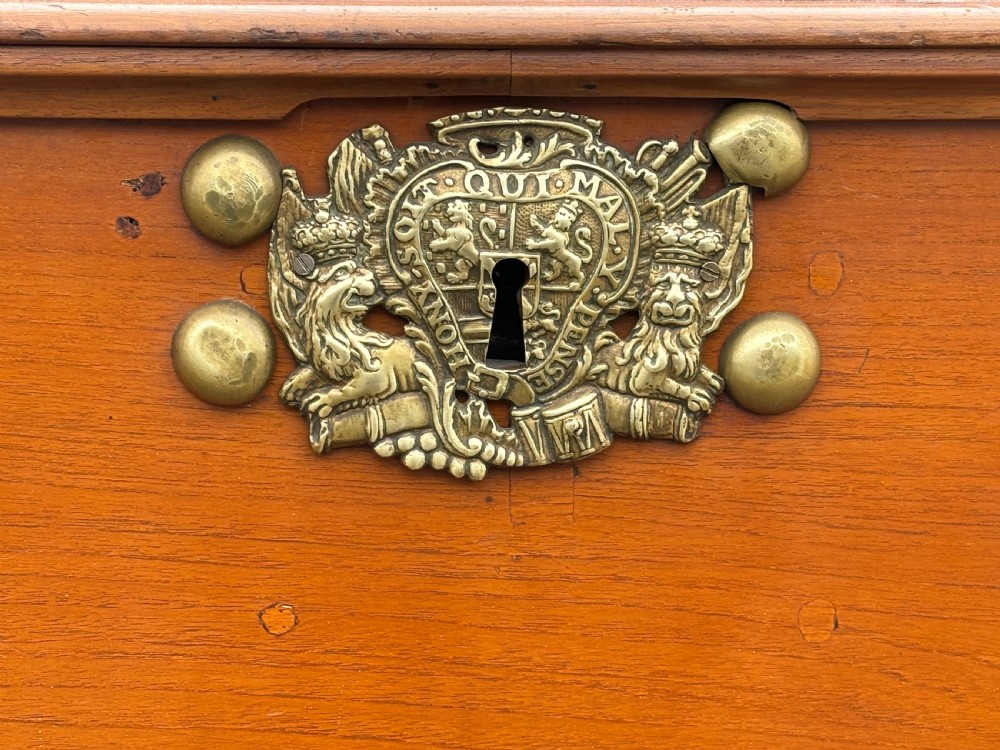 An 18th-century warm brown walnut colonial chest featuring brass corner brackets, a central decorative brass escutcheon, lid studs, and dark turned bun feet. View X