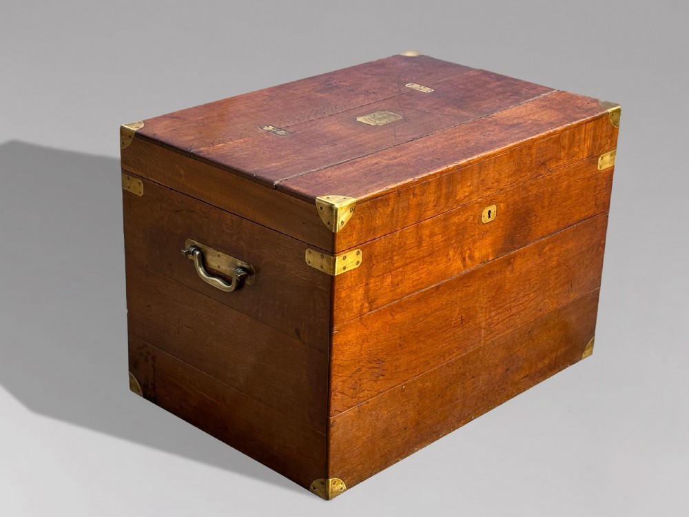 A large rectangular 19th-century oak travelling trunk featuring brass corner mounts, drop side handles, and an inlaid lid cartouche.