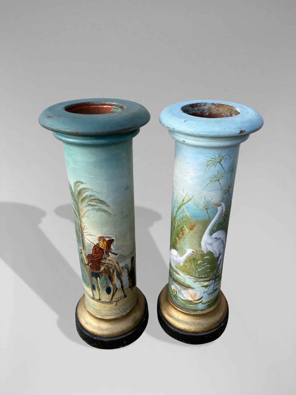 A pair of 19th-century French hand-painted cylindrical wooden columns featuring narrative desert and riverbank scenes above turned gilded bases. View II