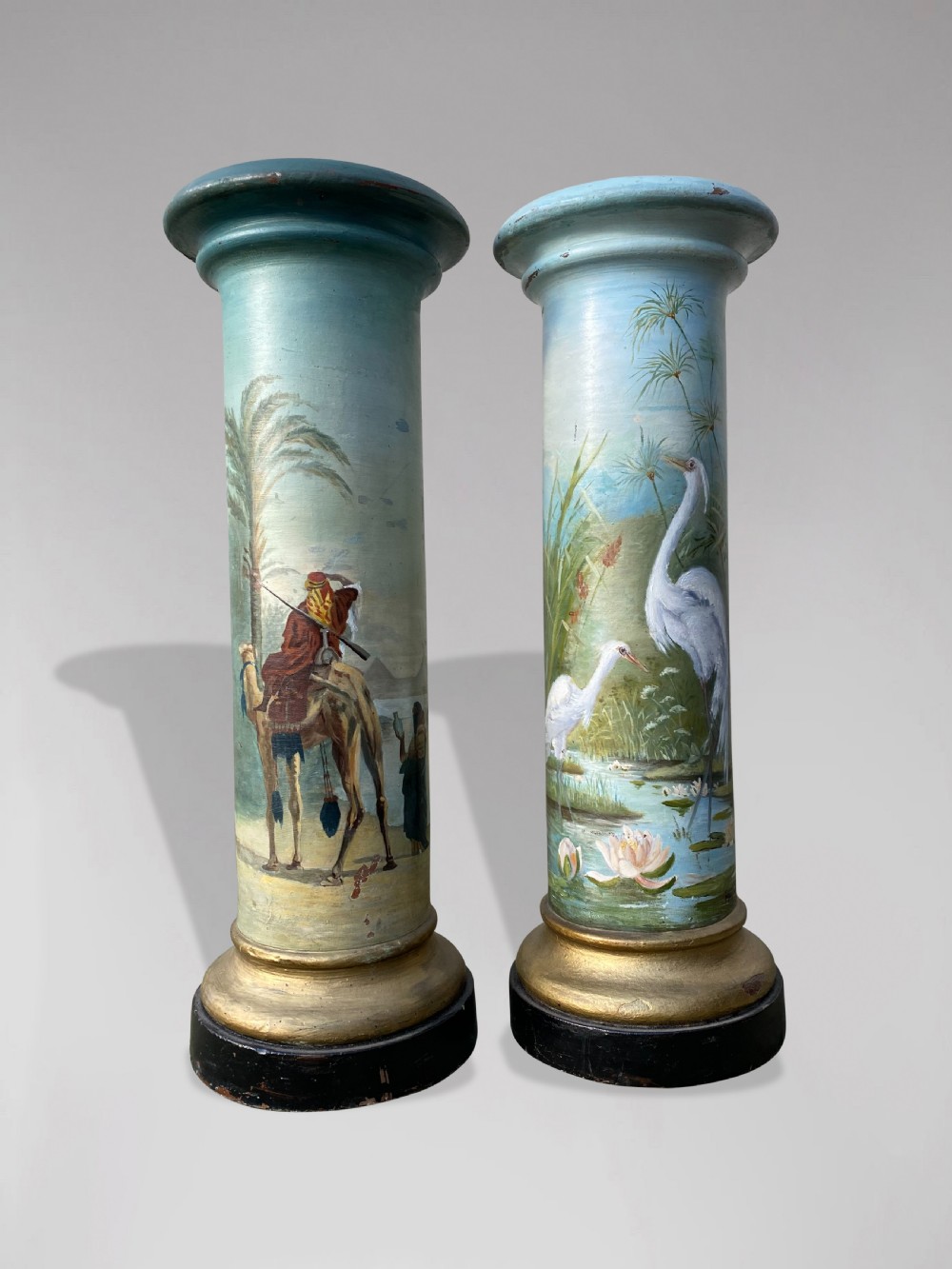 A pair of 19th-century French hand-painted cylindrical wooden columns featuring narrative desert and riverbank scenes above turned gilded bases. View IX