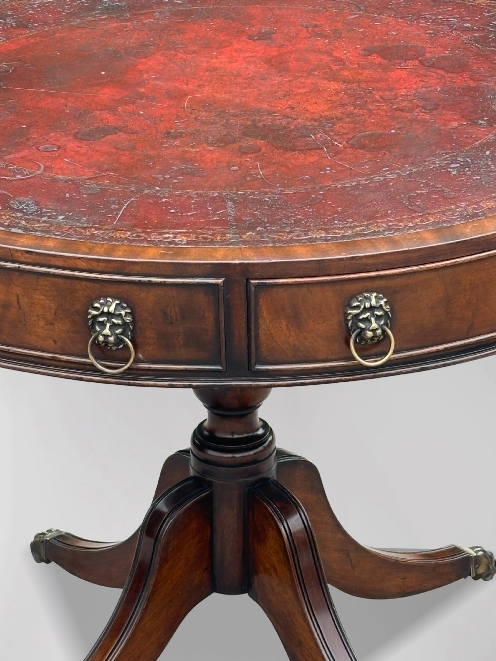 A 19th-century circular mahogany drum table featuring a red leather inlaid top, brass lion mask handles on perimeter drawers, and a pedestal base on splayed legs with brass paw castors. View III