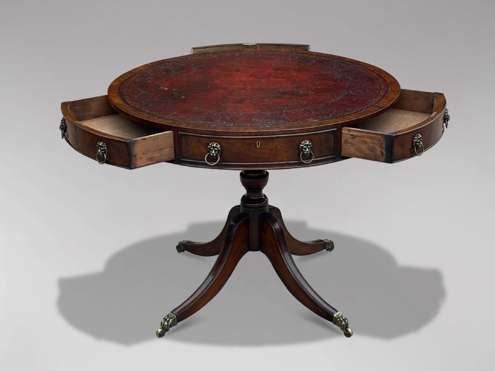 A 19th-century circular mahogany drum table featuring a red leather inlaid top, brass lion mask handles on perimeter drawers, and a pedestal base on splayed legs with brass paw castors. View IV