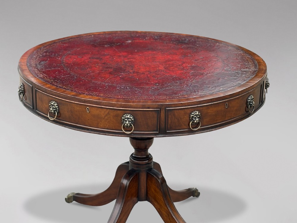 A 19th-century circular mahogany drum table featuring a red leather inlaid top, brass lion mask handles on perimeter drawers, and a pedestal base on splayed legs with brass paw castors. View VI