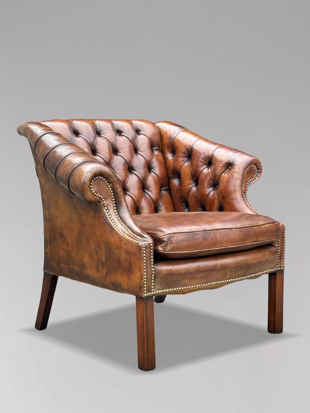 A 19th-century brown leather club armchair featuring deep button tufting, rolled arms with brass studding, and tapered timber legs.