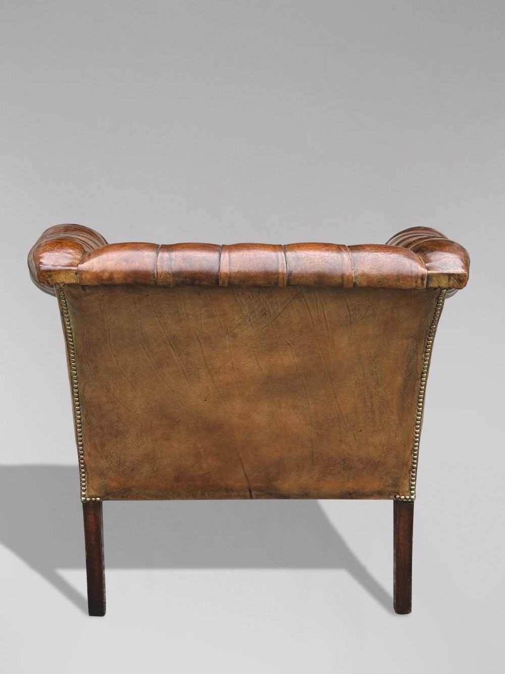A 19th-century brown leather club armchair featuring deep button tufting, rolled arms with brass studding, and tapered timber legs. View III