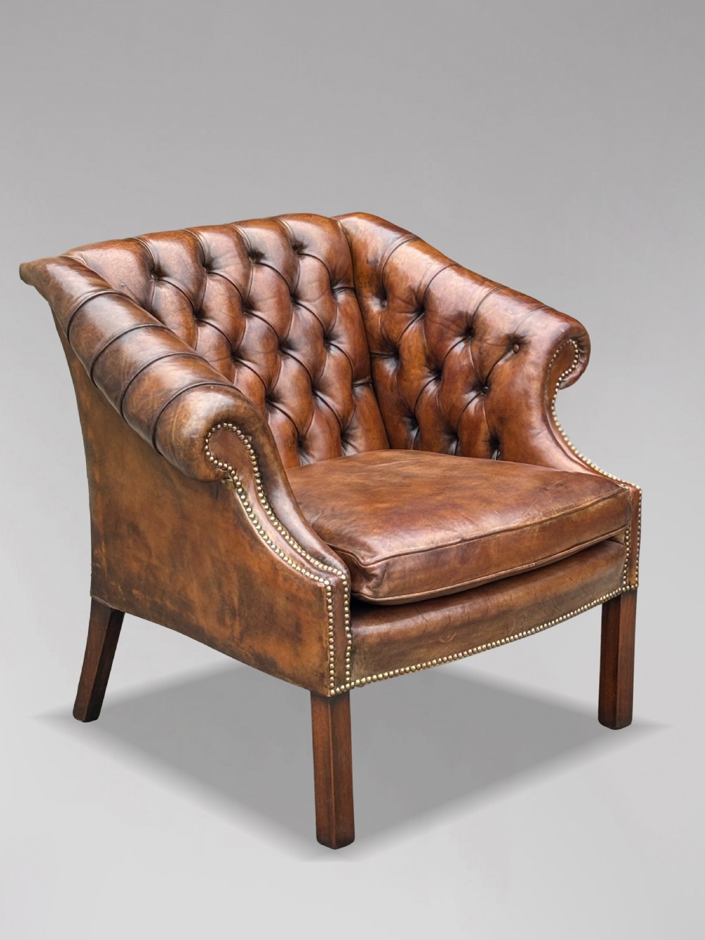 A 19th-century brown leather club armchair featuring deep button tufting, rolled arms with brass studding, and tapered timber legs. View VI