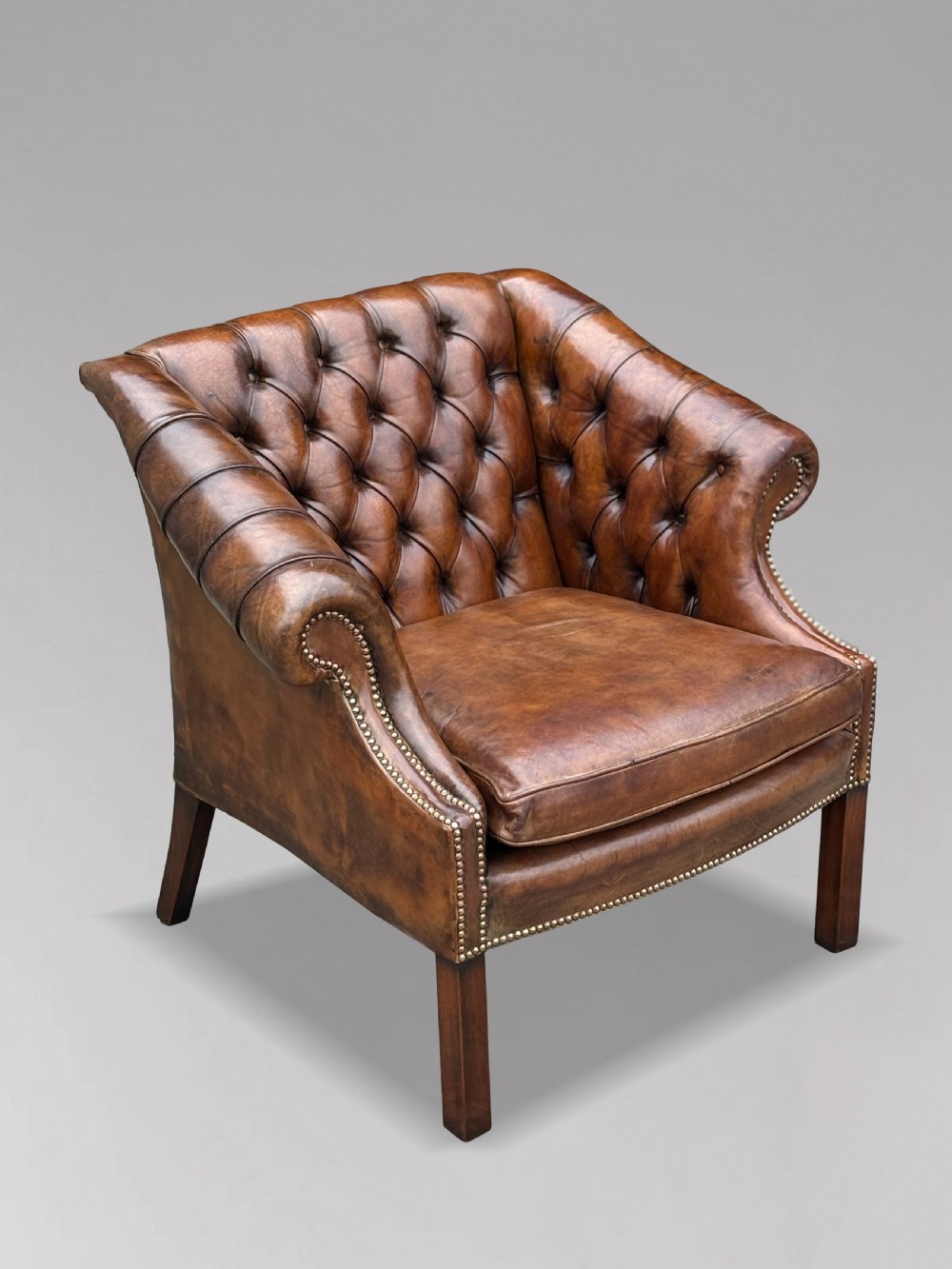 A 19th-century brown leather club armchair featuring deep button tufting, rolled arms with brass studding, and tapered timber legs. View IX