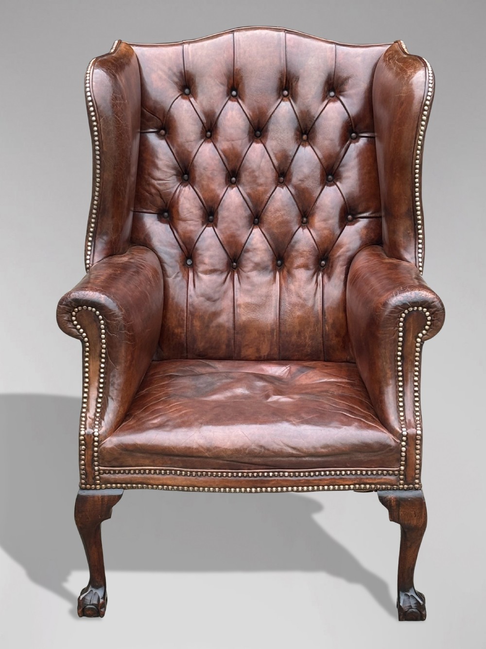 A 19th-century deep brown leather wingback armchair featuring a button-tufted backrest, brass stud trim, and hand-carved mahogany cabriole legs with ball-and-claw feet. View II