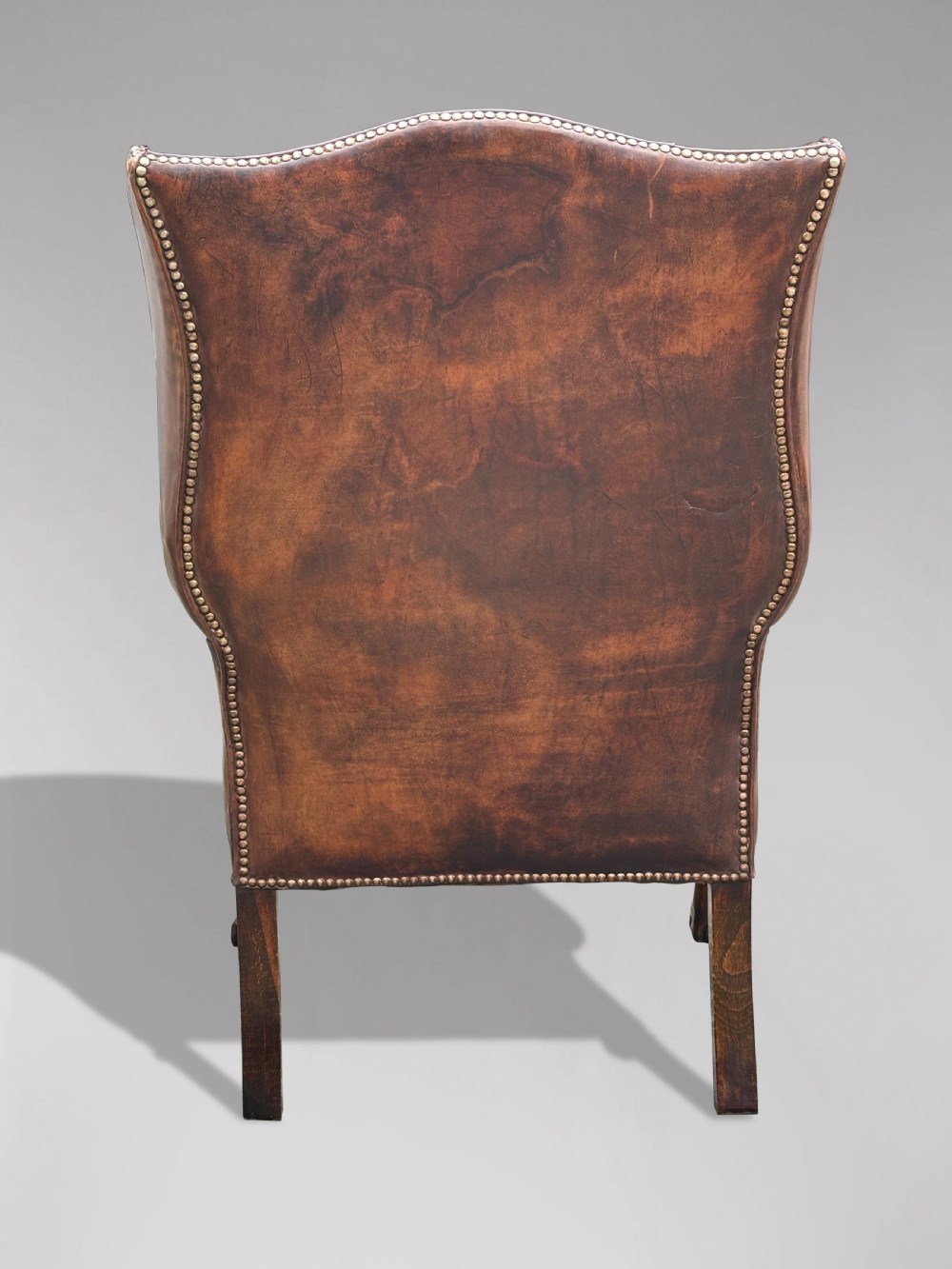 A 19th-century deep brown leather wingback armchair featuring a button-tufted backrest, brass stud trim, and hand-carved mahogany cabriole legs with ball-and-claw feet. View III